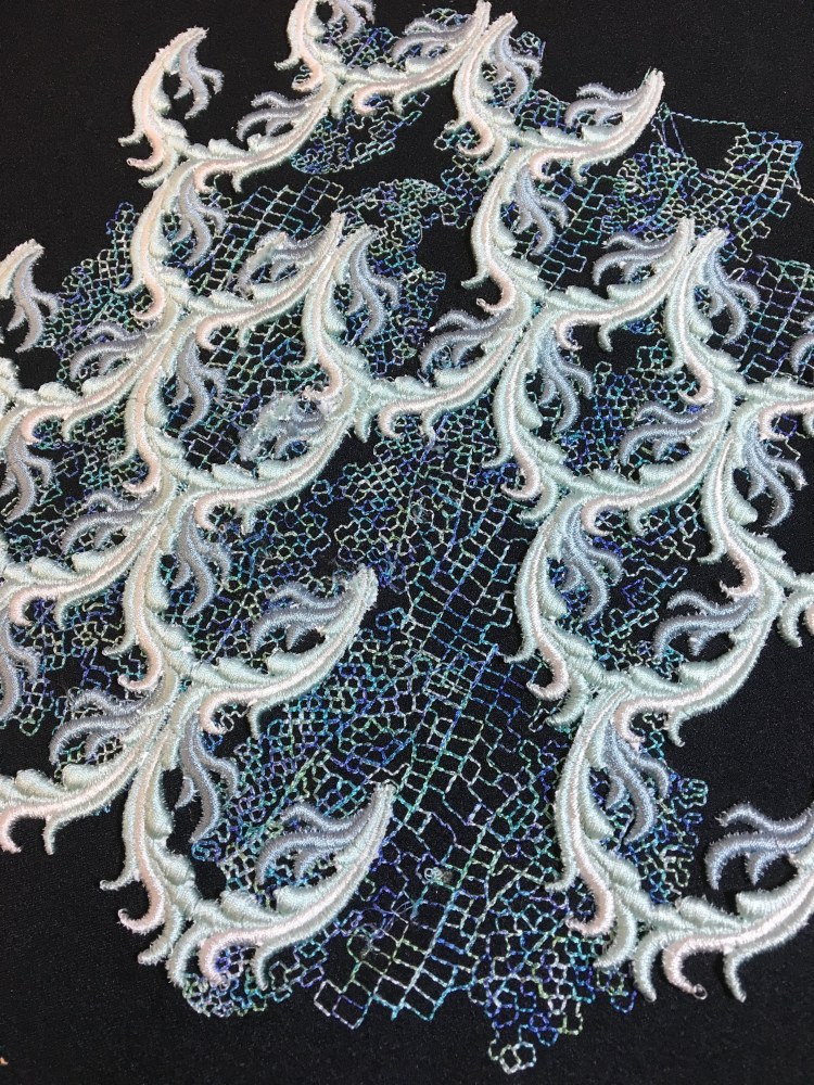 Blue Ombre threads used for the running stitch underneath raised satin stitch fronds set out in a broken scales pattern on dark navy fabric 