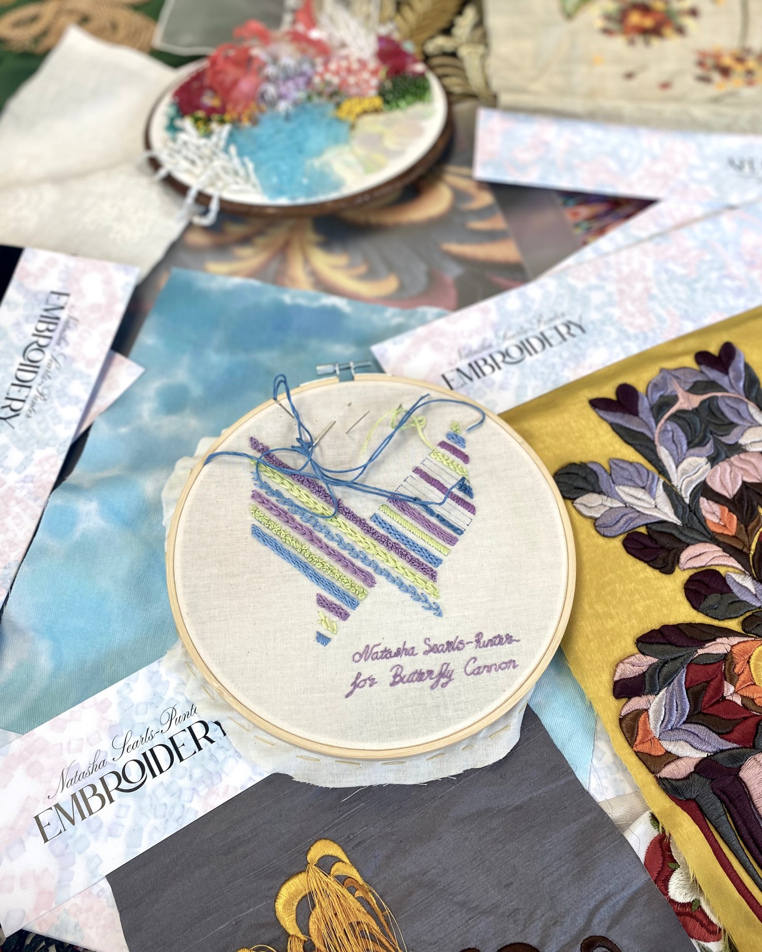 Hand Embroidered Butterfly Cannon Logo on canvas fabric, resting on a bed of scattered fabric samples