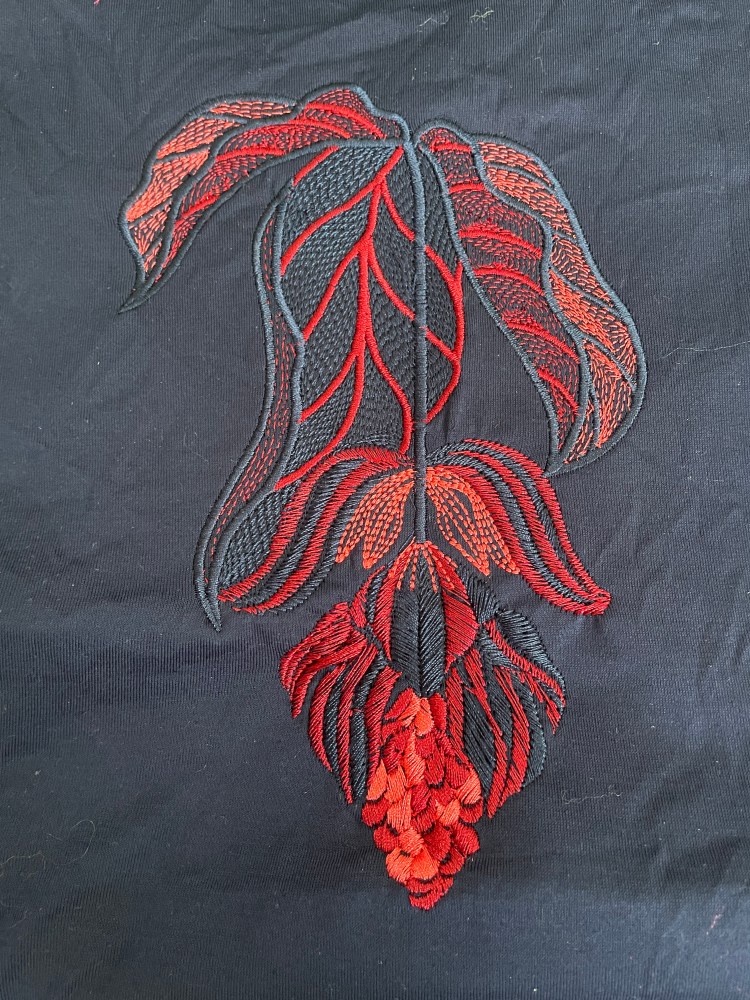 A detailed photo of the medinilla design embroidered onto navy fabric as a sample in red, pink and navy machine embroidery threads