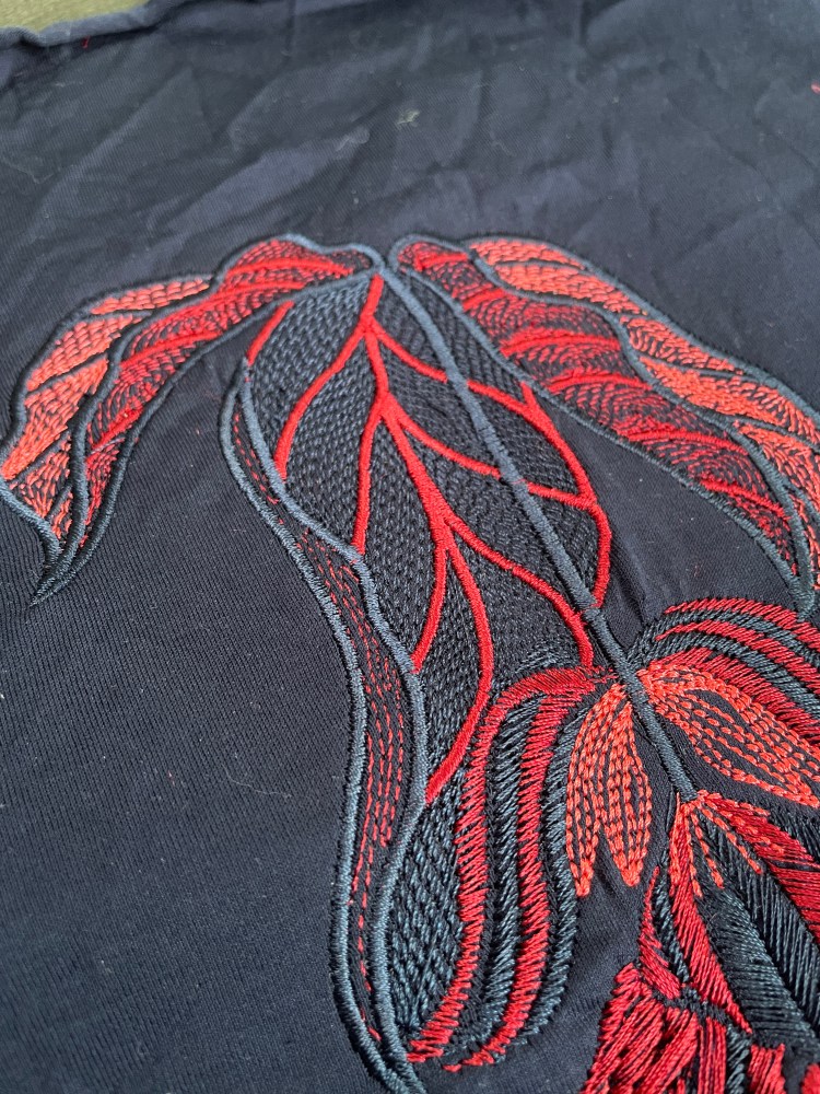 A detailed photo of the medinilla design embroidered onto navy fabric as a sample in red, pink and navy machine embroidery threads