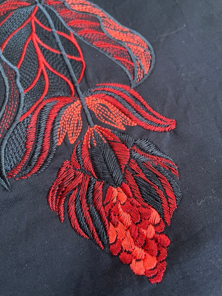 A detailed photo of the medinilla design embroidered onto navy fabric as a sample in red, pink and navy machine embroidery threads