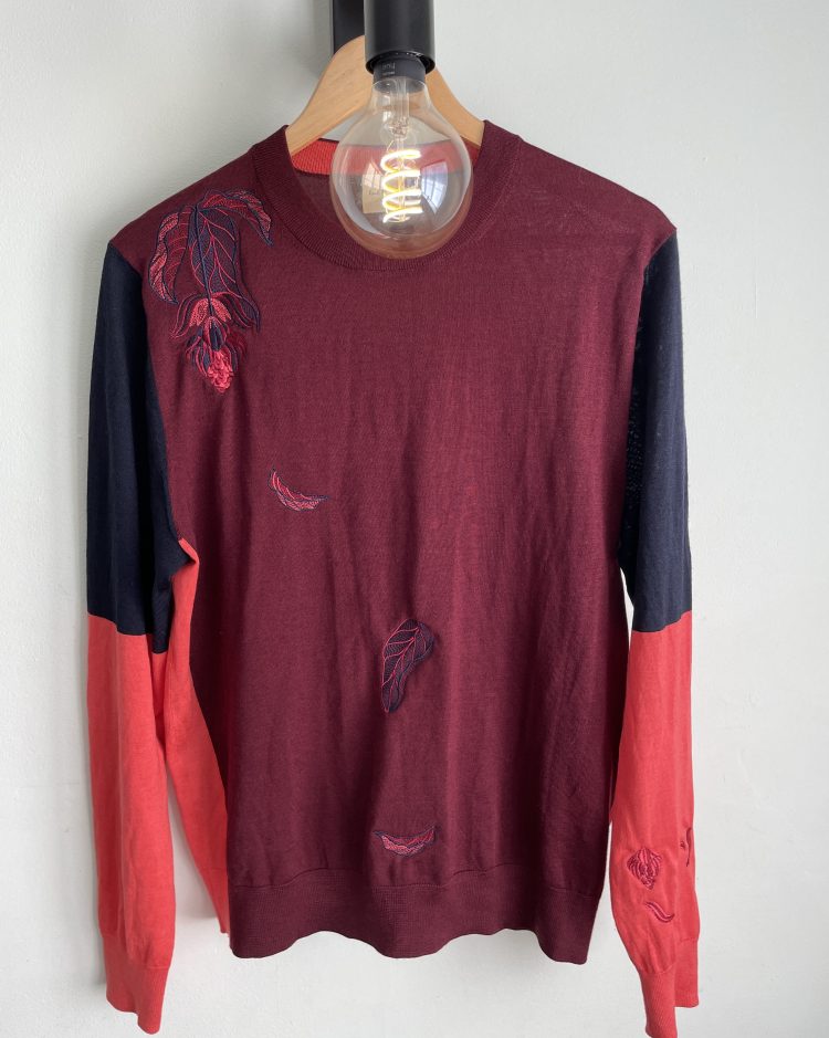 Burgundy jumper with navy and pink sleeves with a large Medinilla flower on the shoulder and leaves floating down from it across the boat and left sleeve in embroidery