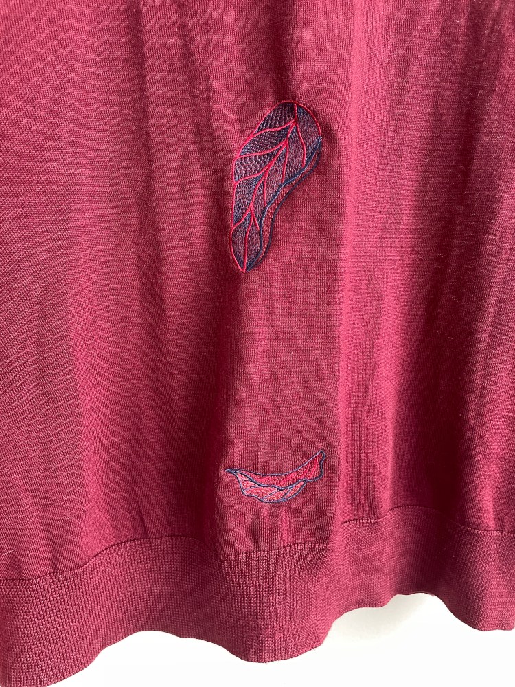 tropical flower leaves in red, blue and pink embroidered onto a burgundy fine knit jumper