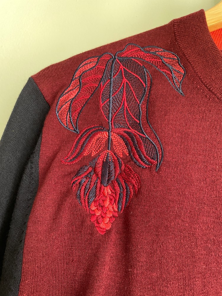 Medinilla flower in red, blue and pink embroidered onto a burgundy fine knit jumper